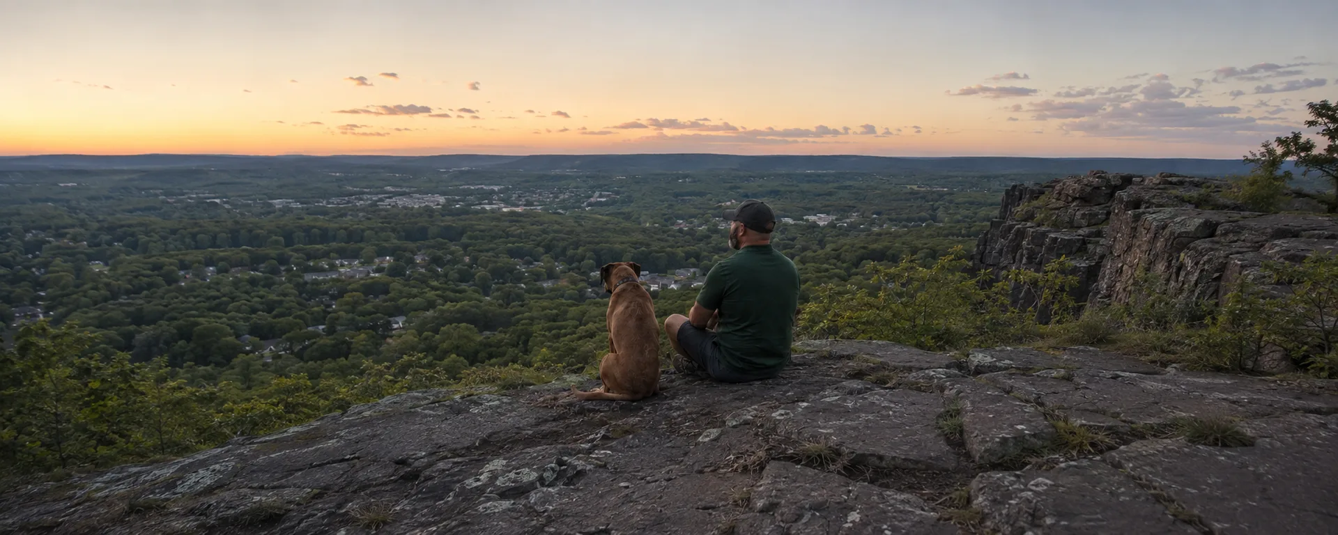 Jason and his dog Max sitting on a rocky overlook above a Connecticut valley at sunset
